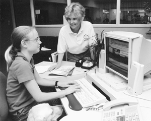 Sheryl Burgstahler advises a DO-IT Ambassador while she works on her computer in an office setting. Photo of DO-IT Director Sheryl Burgstahler advises a DO-IT Ambassador while she works on her computer in an office setting.
