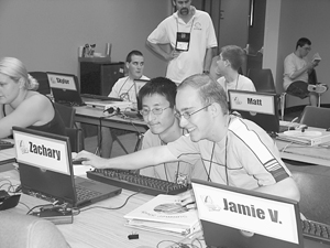 Photo of student on the left helps student on the right with mouse operation,