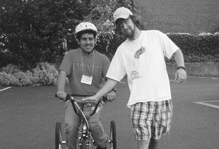 Picture of DO-IT Phase II Scholar Israel on a bike with DO-IT staff member James holding the handlebars.