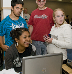 Photo of several students gather around a laptop