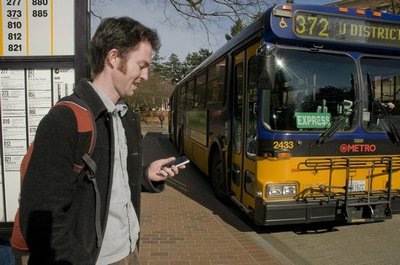 A person using a phone while a bus pulls up to the stop