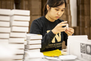 A woman in a University of Washington sweatshirt places a label on a test tube.