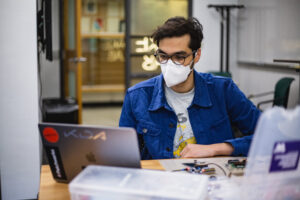 A man in a medical mask works at a laptop