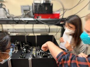 Scientists gather around laser table equipment to make adjustments