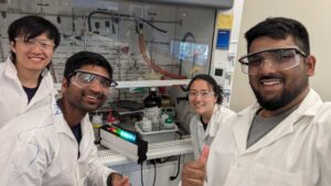 A group photo of four student scientists in lab coats featuring a diverse mix of men and women 